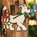 Colorful cartoon dog sign featuring vibrant flowers outdoors in a warm setting.