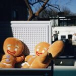 Large gingerbread man plush toys in sunlight, outdoors, near white building.